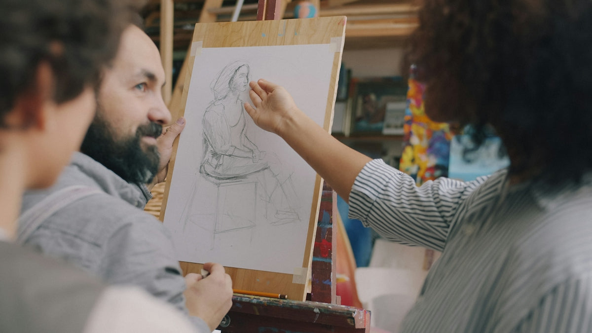A person gesturing toward a pencil sketch of a seated figure on an easel
